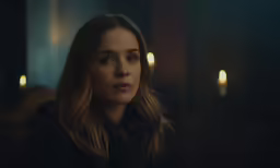 a girl is staring intently while candles shine in the background