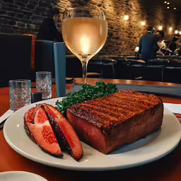 a plate filled with steak and fruit next to glasses of wine