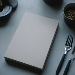 a blank book next to two forks and spoons