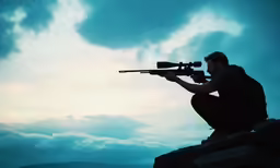 man aiming at a weapon while sitting on top of a hill