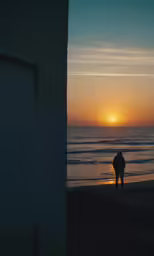 a silhouette of a person standing at the beach during a sunset