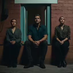 three people that are sitting against a wall