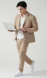 a man in tan suit walking while using a laptop