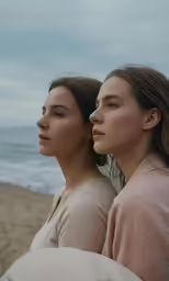 two women, one with hair blowing back on the wind, the other facing in the distance