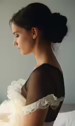 a woman wearing a dress sits in bed looking away
