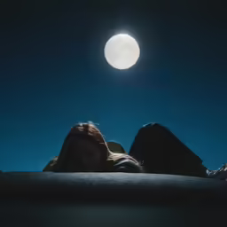 two people are laying in a bed under a full moon