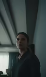 the woman is wearing a grey shirt standing in the room
