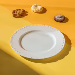 an oval white plate on a yellow and yellow colored table,an image of a plate and some pastries on table