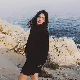 a woman wearing a black sweater dress on the beach