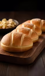 rolls lined up on a wooden board next to bowl of crackers