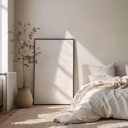 a bedroom with a bed, light, plant, radiator, a painting, pillows and blankets on the floor