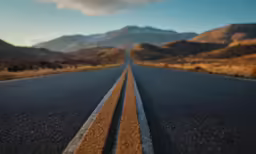 a black asphalt road with yellow lines and hills in the background