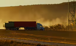 semi truck driving on road at sunset,a red and green semi truck drives on the road