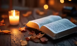 the book is lying on the table next to the candle
