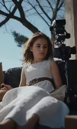 a girl with brown hair in white is next to a video camera