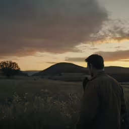 a man walking across a lush green field at sunset