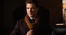 a person in a suit holding a brown scarf around their neck