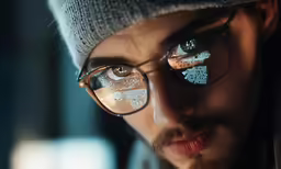 man with eye glasses and hat looking in mirror