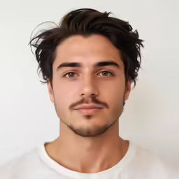 a young man with long hair and goatee standing in front of white background
