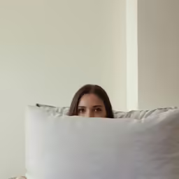a woman hiding behind the covers and covering herself with the pillow