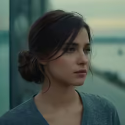 the woman is looking at something while she stands near water