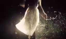 a woman walking through tall grass in the dark
