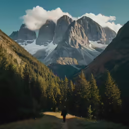 man walking up the road towards mountains under cloudy skies