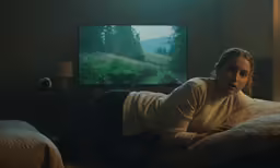 the woman is laying down on the couch watching television