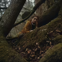 a woman sitting on a mossy tree trunk near many leaves