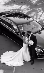 a black and white photo of a bride and groom standing next to their car