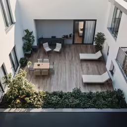a rooftop with chairs, table and plants on the top floor
