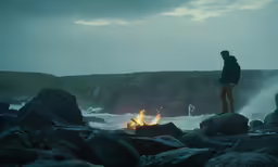 a man is standing by some rocks and a fire