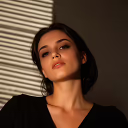 a close - up photo of a woman posing next to some blinds