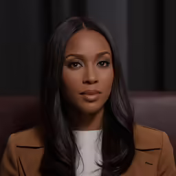 the woman sitting on the brown couch is looking away