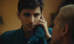 a man talks on a telephone while a person looks in