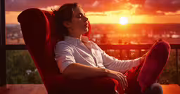 the lady is relaxing on the balcony at sunset,a woman sits on a red chair and looks at the sun