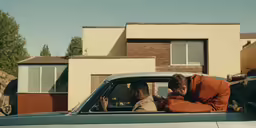 two people sitting in a truck in front of a house