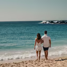 man and woman walking along beach near ocean