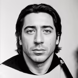 a man with long hair, in a black shirt, looks into the camera