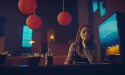 a woman in grey shirt sitting at bar with bottles of alcohol
