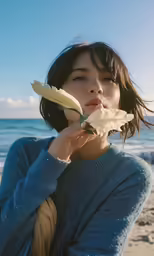 an asian girl holds a flower in front of her face