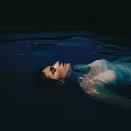 a woman that is laying down in the water,a woman swims through the water with her head tucked into her chest