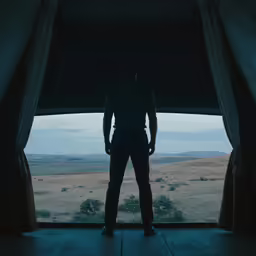a man in a dark room looking at an open window