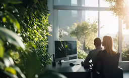 two people sit in a office looking at a large monitor