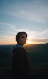 a person standing on a hill looking down at the sunset