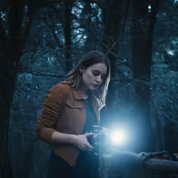 a young woman holding up a flashlight in a forest