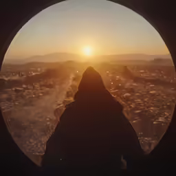view through a circular window into an expanse of land and mountains at sunset