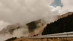 the mountains are covered with fog next to a road