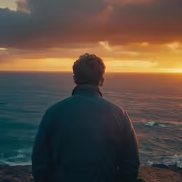 man watching the sunset over the ocean with stormy skies
