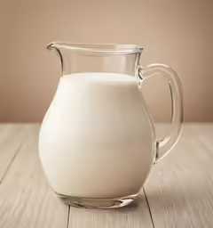 a glass jug of milk on a wooden table